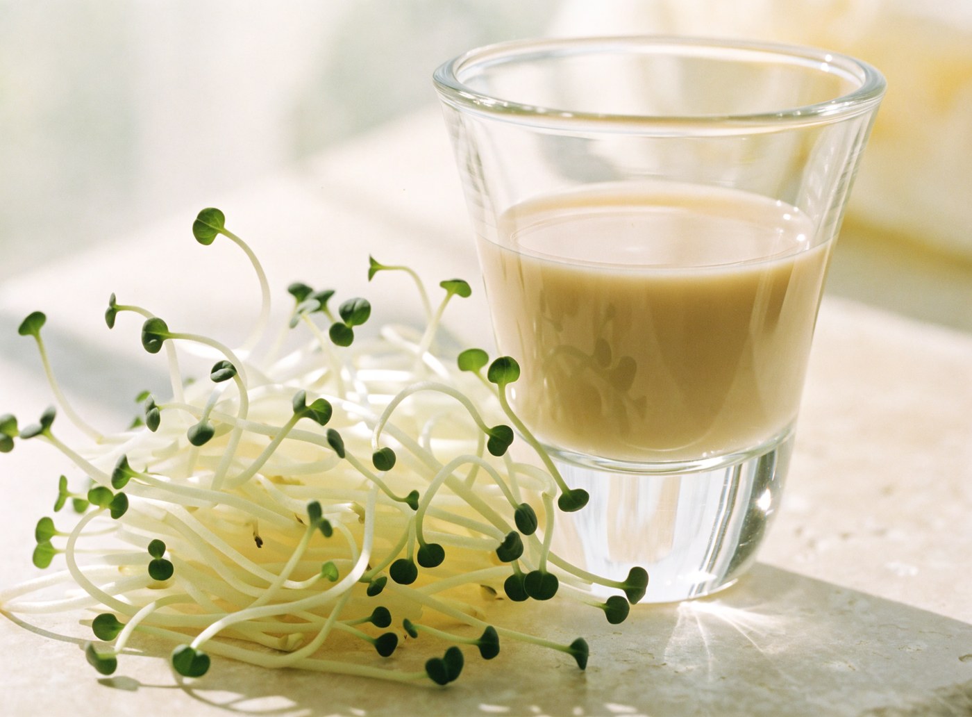 Shots of vivid green broccoli sprout juice beside fresh sprouts