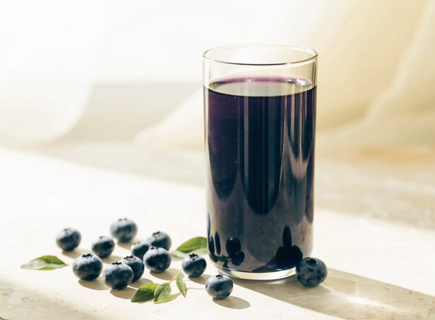 A glass of deep purple bilberry juice beside fresh bilberries