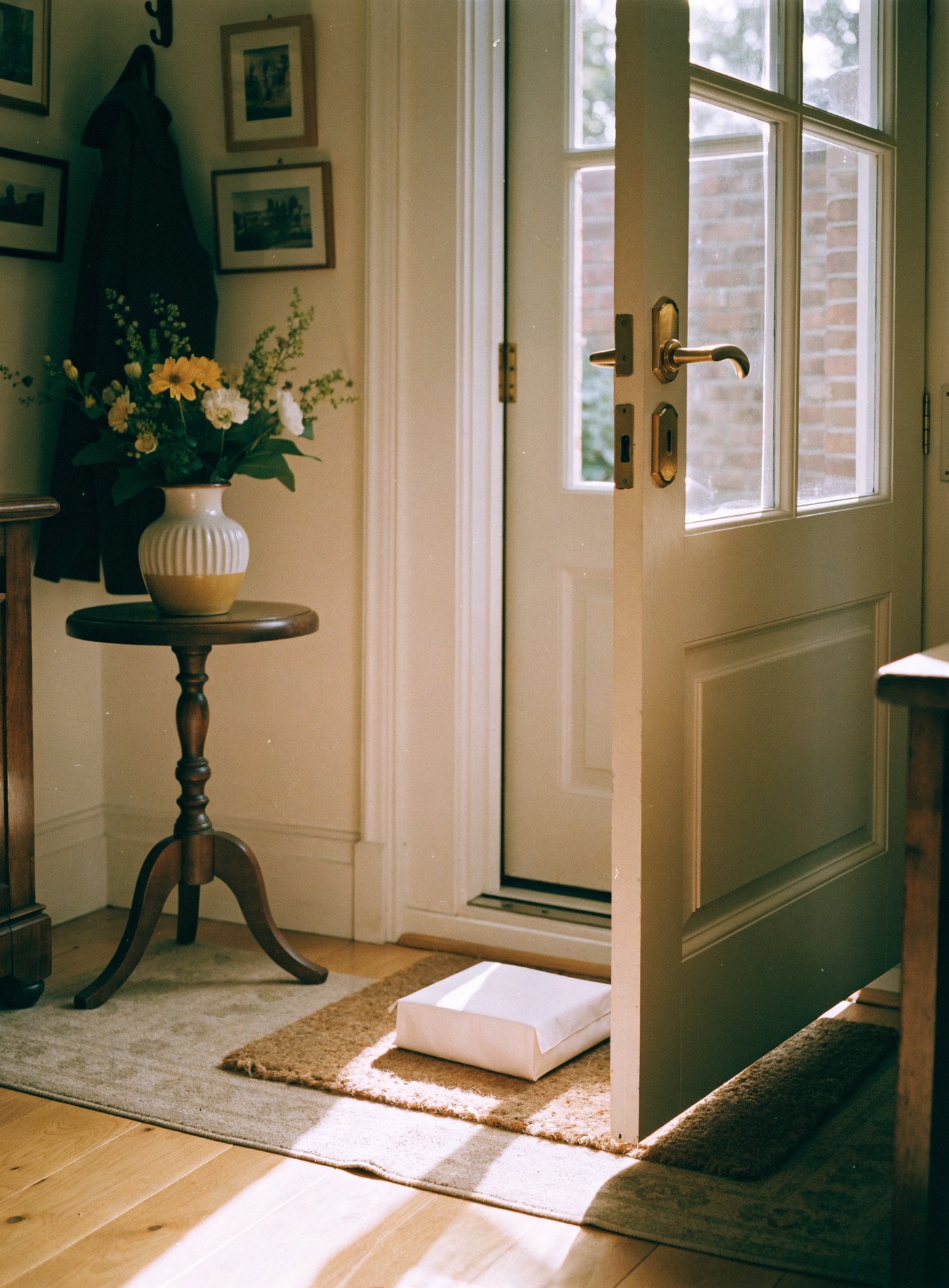 Hands picking up a small parcel from the doormat of a sunlit hallway