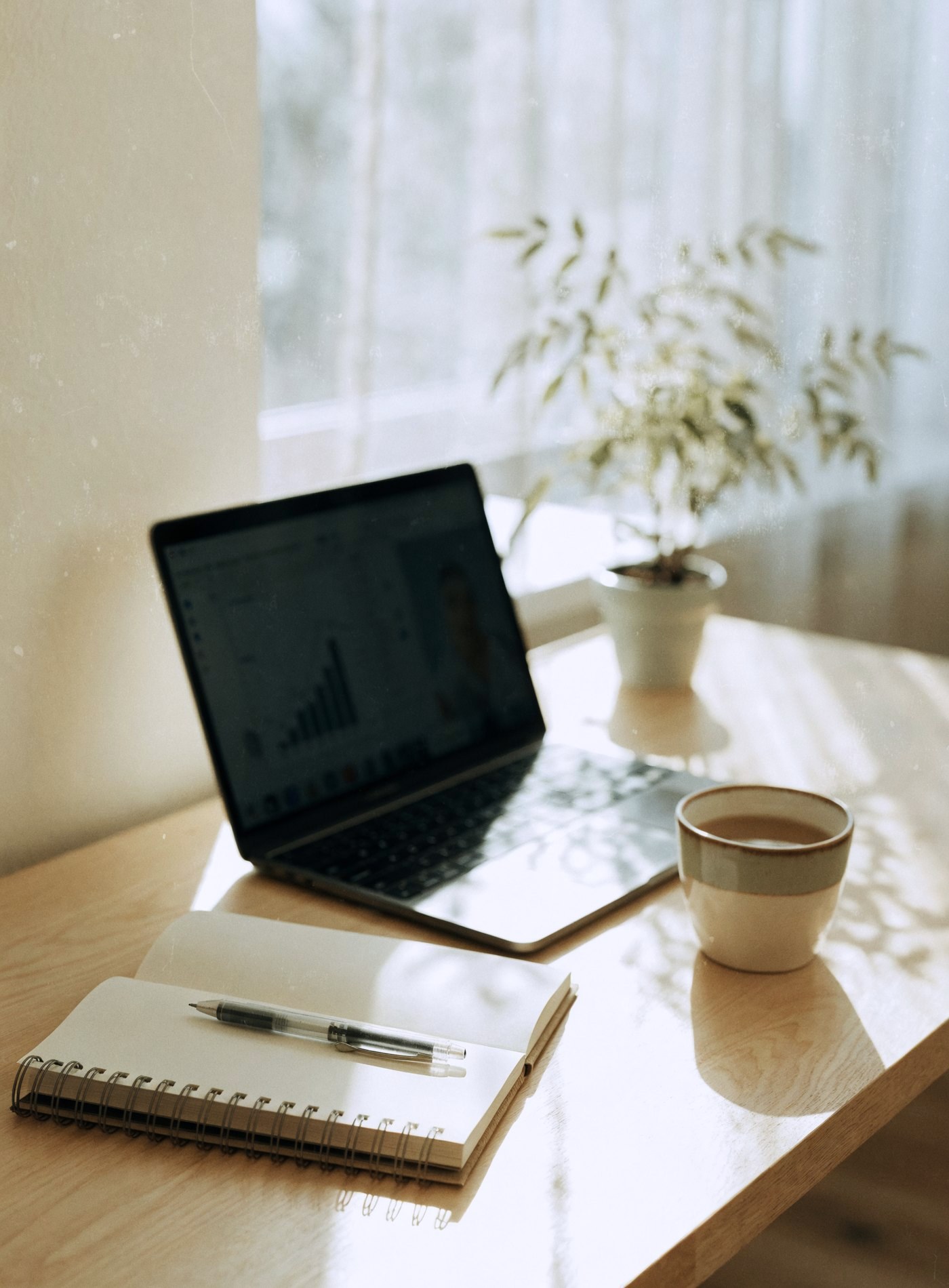 A laptop showing a results chart on a video call, with a notebook and tea beside it