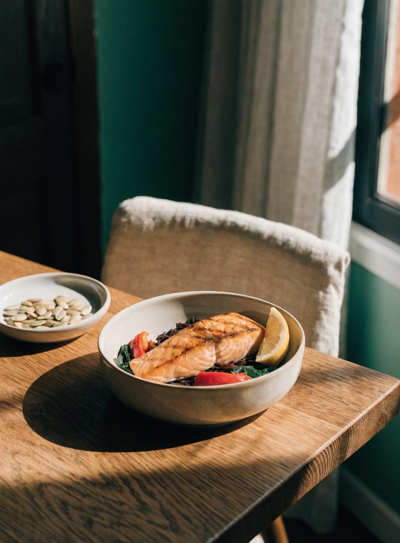 A bowl of grilled salmon, wild rice, peppers and spinach on an oak table